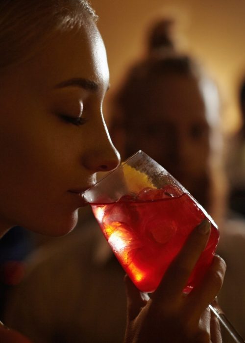 Close-up profile of glamorous blonde girl enjoying fresh fruit drink, sitting at bar counter next to
