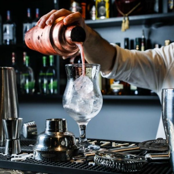 man pouring cocktail from shaker in the glass with ice bar side view